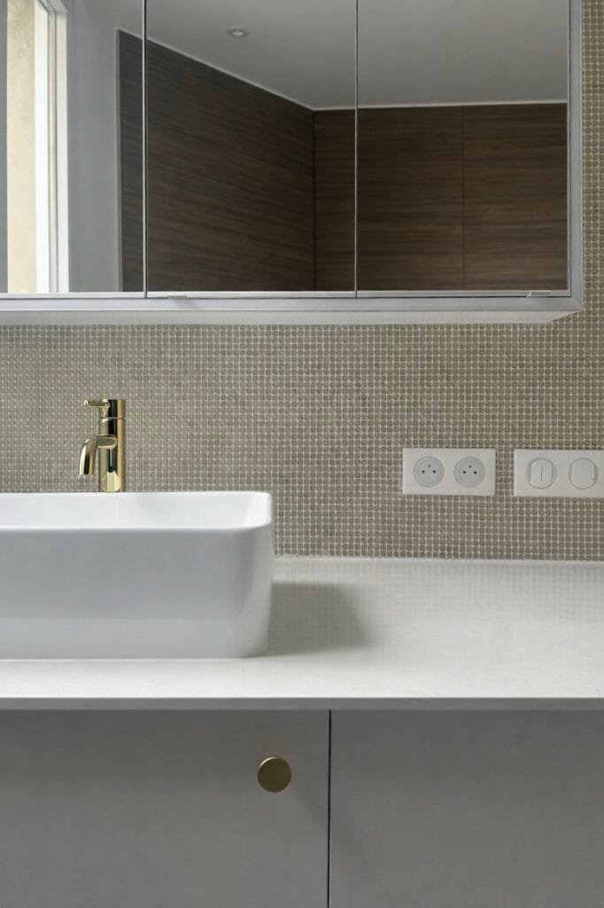 Contemporary bathroom with white rectangular sink, gold faucet, matte gray cabinet and beige mosaic backsplash, elegant and refined interior.