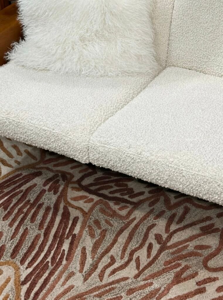 Detail of an ecru bouclé fabric sofa combined with a graphic rug with organic brown and terracotta patterns, contemporary interior focused on materials and textures.