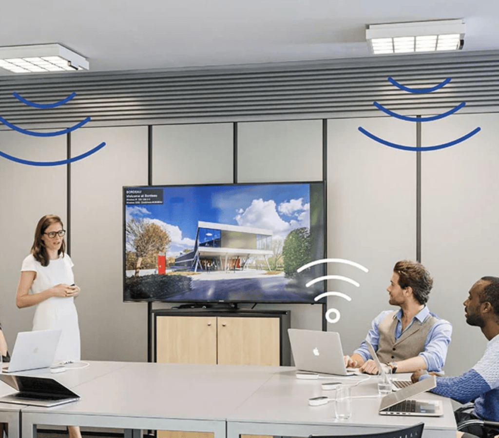 Salle de réunion équipée de la technologie LiFi Trulifi de Signify, transmettant des données via la lumière LED pour une connexion sécurisée et haut débit, avec collaborateurs utilisant ordinateurs portables.