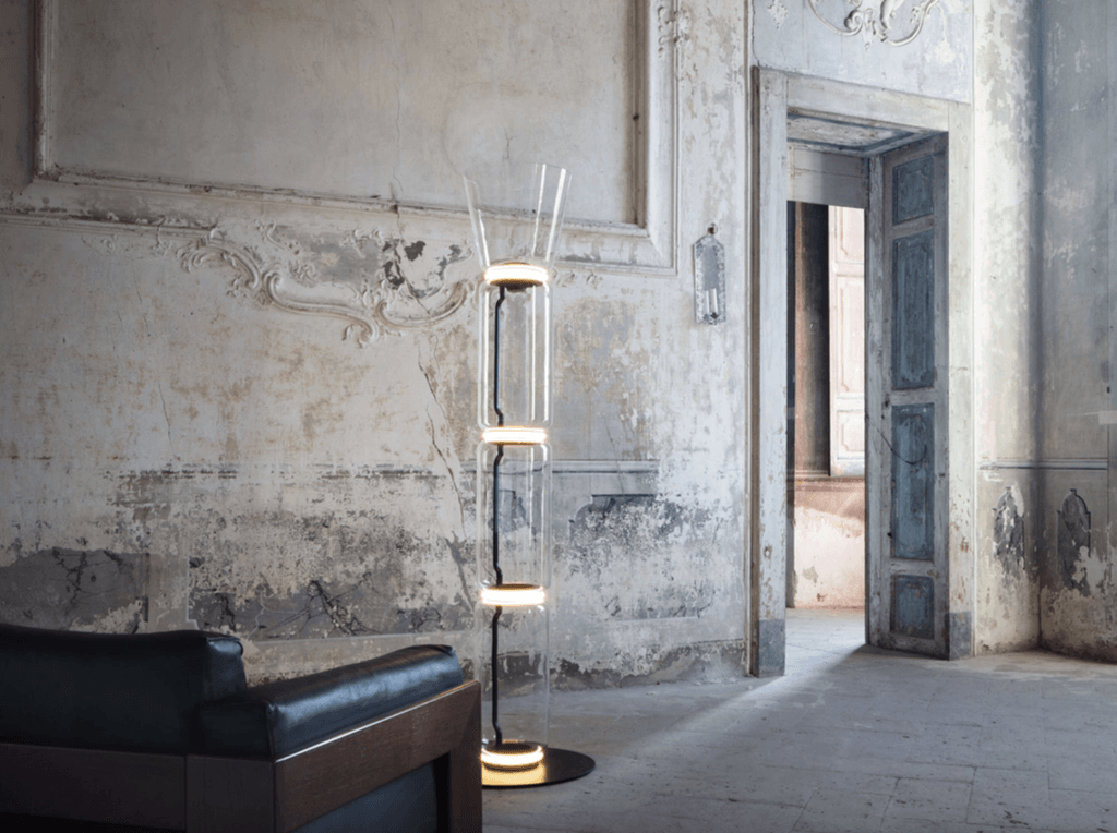 Lampadaire Noctambule de Flos dans un intérieur ancien patiné, colonne en verre soufflé avec anneaux LED lumineux, design de Konstantin Grcic, ambiance contemporaine et sculpturale.