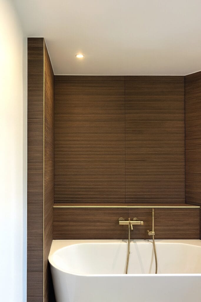 Designer bathroom with white freestanding bathtub, wall-mounted brass faucet, ribbed wood panels and discreet lighting, elegant and soothing contemporary interior.