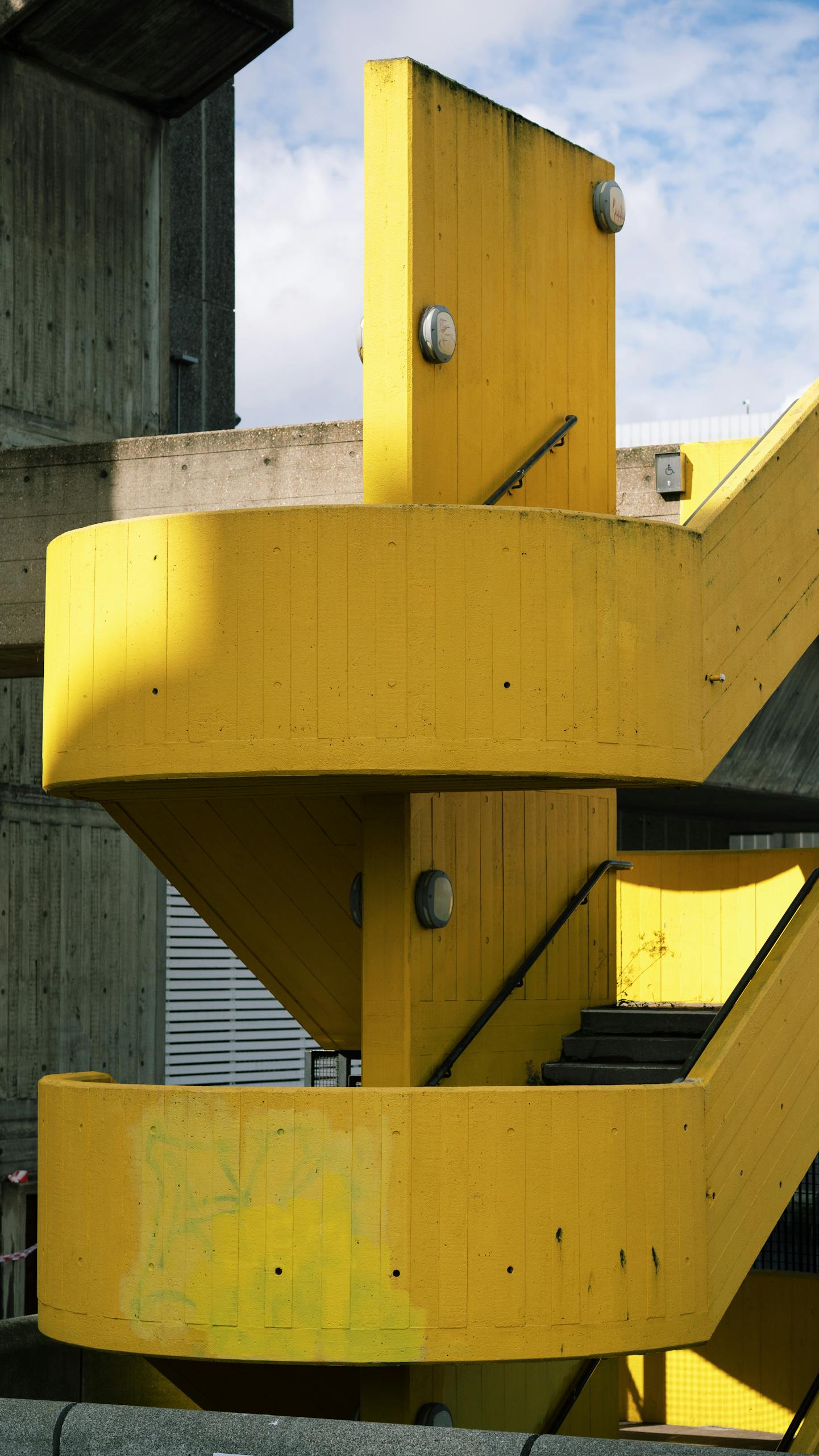 Striking yellow spiral staircase contrasting with concrete backdrop.